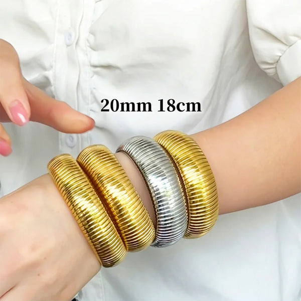 A wrist wearing a stack of gold and silver elastic bangle bracelets on a white shirt sleeve.