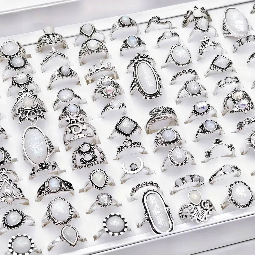 A collection of silver and white stone charm rings displayed in a white tray.