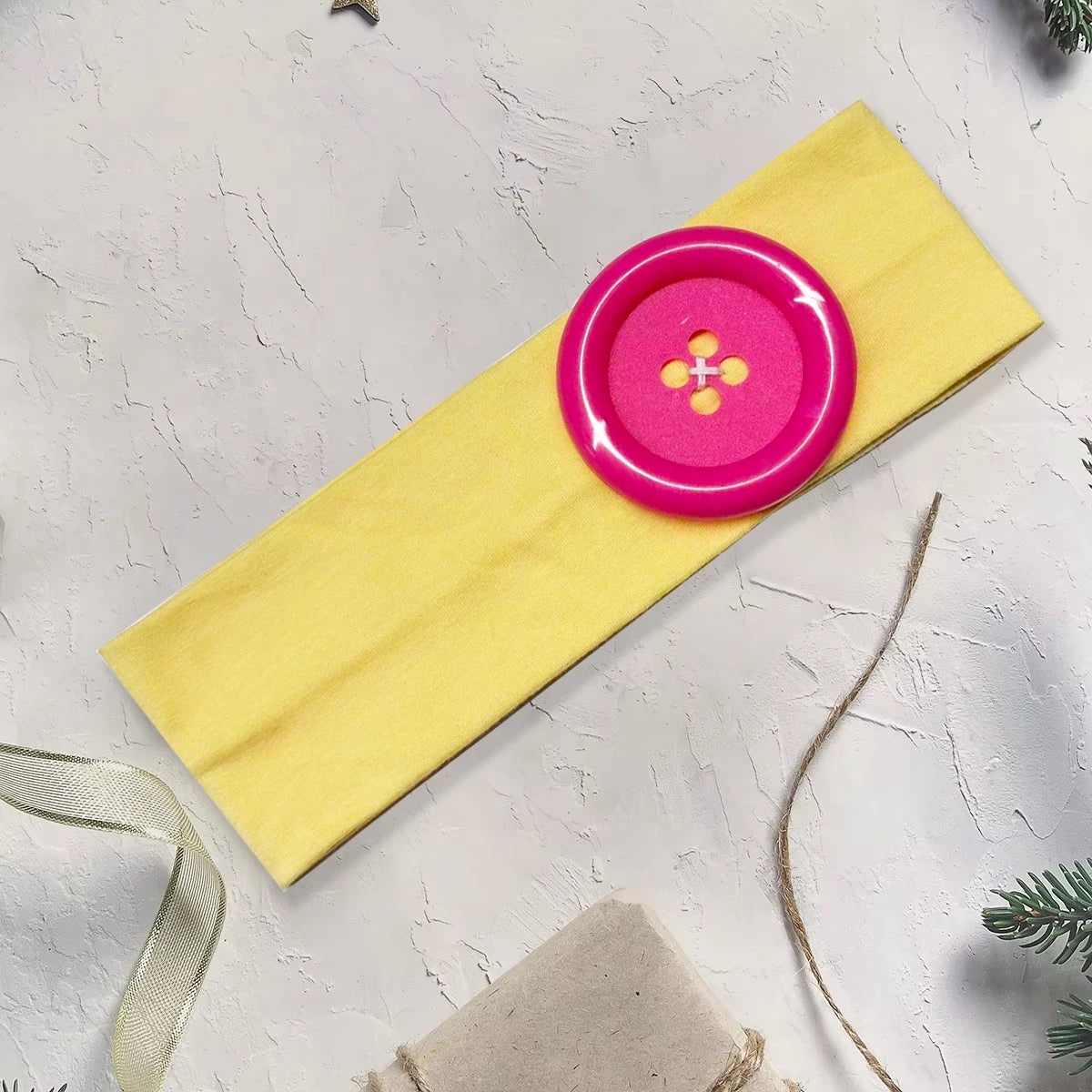 Yellow fabric hairband with a bright pink button detail and a thin twine string.