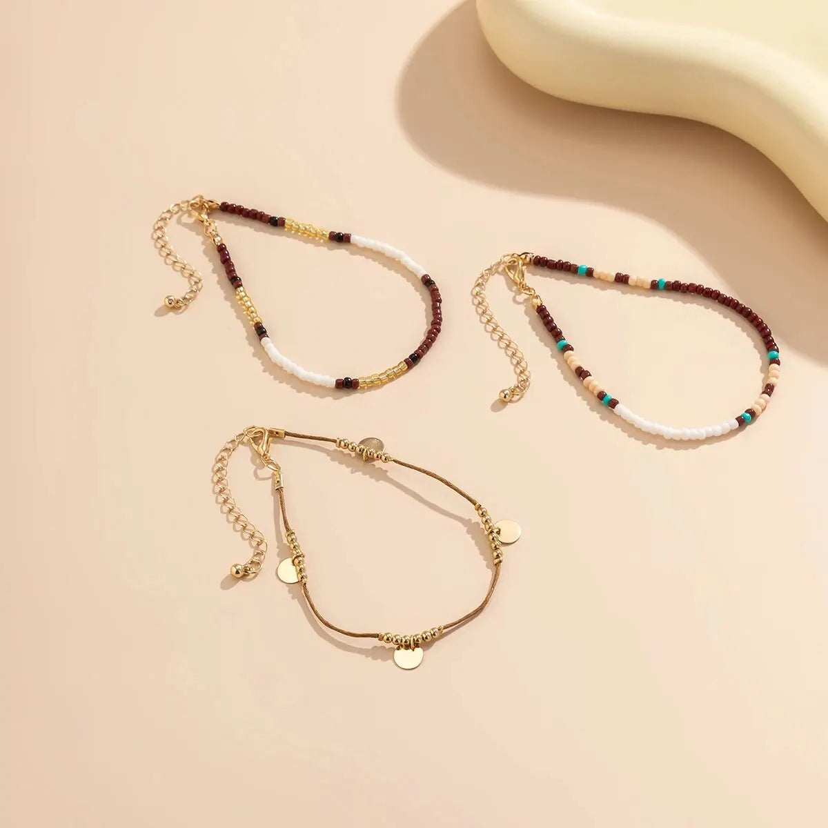 A set of three bohemian anklets featuring various colored and gold seed beads and white pearls displayed on a neutral backgro