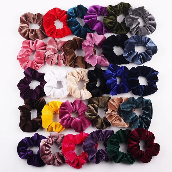 A collection of six velvet scrunchies in various shades including red, purple, green, and brown.