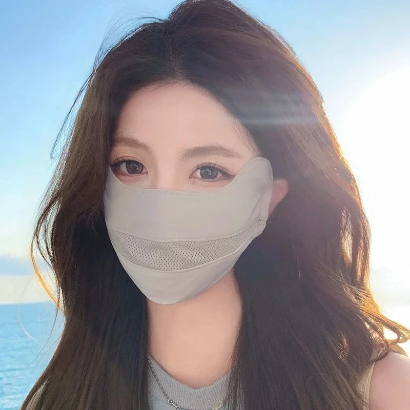 A woman wearing a light gray breathable ice silk UV protection face mask against a bright, sunny sky and ocean background.