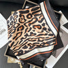 A black silk scarf featuring a leopard print in shades of brown and beige, displayed on a dark surface.