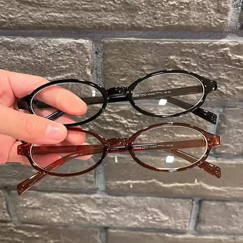 Une main tient une paire de lunettes à ovales rétro brun-tintées sur un fond de briques grises.