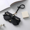 A black leather pouch with a gold chain and black strap is shown next to a white box.