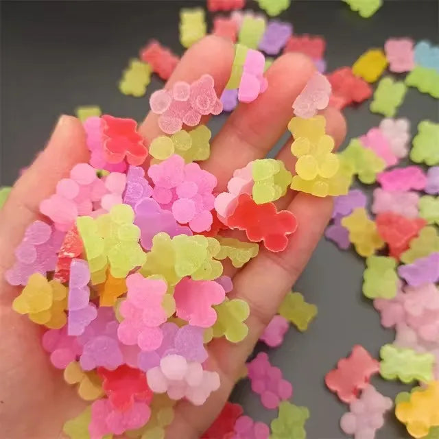 A hand holds a collection of colorful resin nail art charms in various shades of pink, yellow, and green.