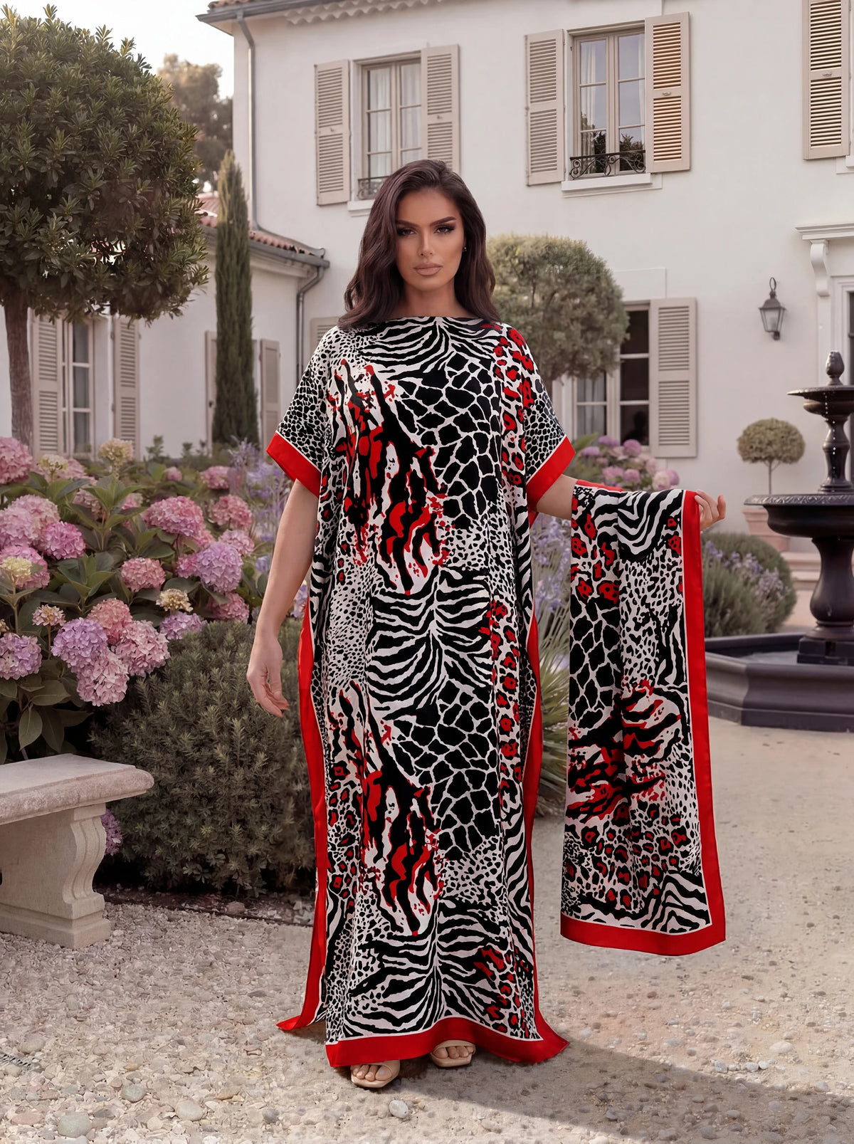 A woman models a black and red leopard zebra print maxi kaftan outdoors in a garden setting.