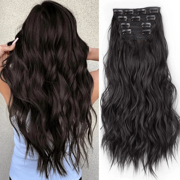 A close-up of long, dark wavy hair extensions with a black clip-in hair piece visible on top.
