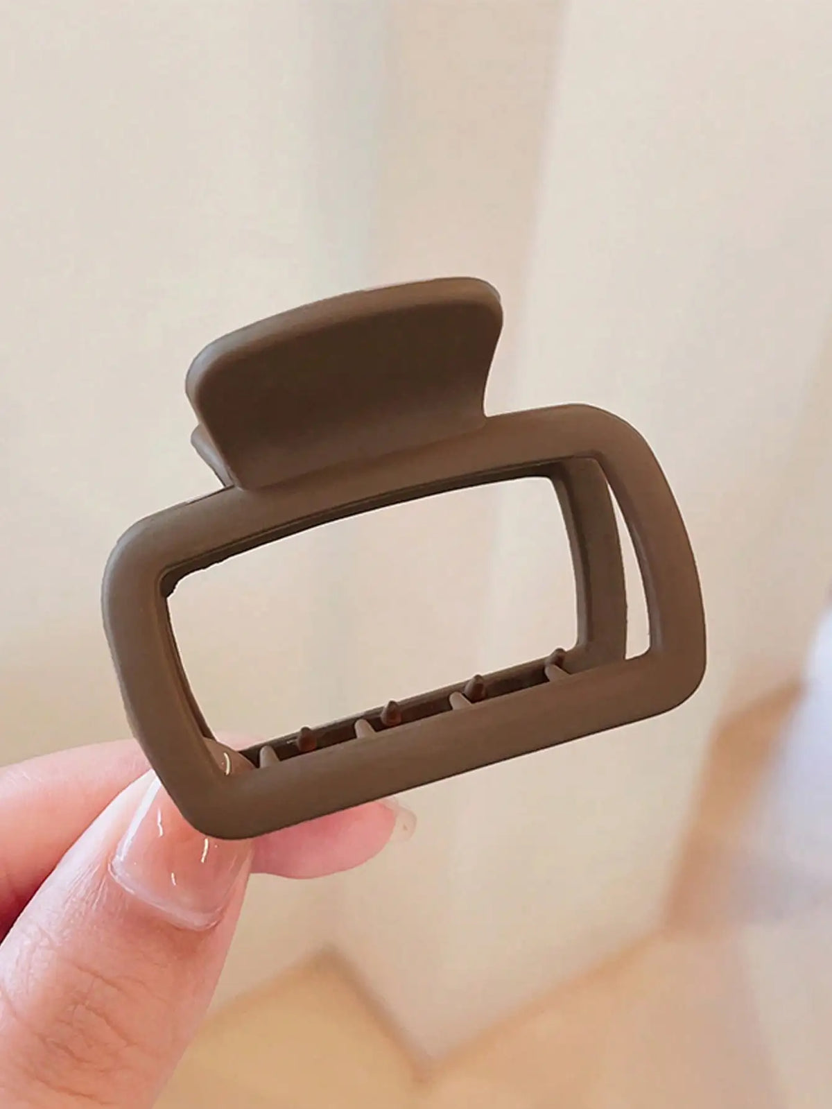 A close-up of a single square lightweight hair claw clip in a matte olive green color being held by a hand.