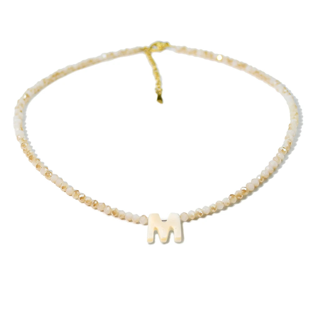 A delicate gold necklace featuring a mother of pearl chain with crystal accents and a letter M pendant.