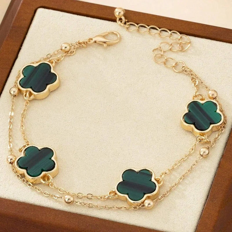 Gold jewelry featuring five-leaf clover charms on a delicate chain anklet displayed on a brown box.