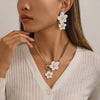 A close-up of a woman wearing a gold floral pendant necklace and matching earrings on her neck and ears.