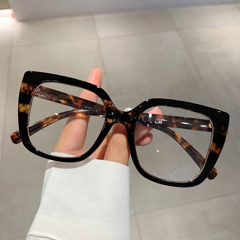 Eine Hand hält eine Paar Schildpattelframes in Tortoise-Muster, quadratische Brillengestelle, vor einem hellen Hintergrund.