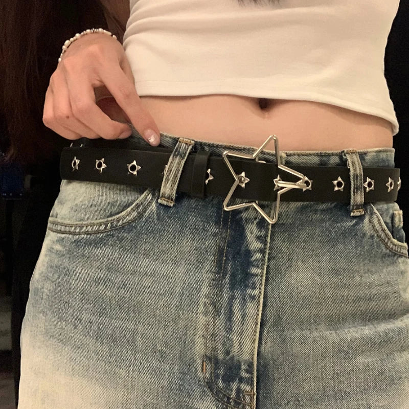 A close-up of a black Y2K punk star riveted belt worn over light wash denim jeans.