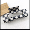 A black and white checkered rectangle hair claw clip resting on a light surface next to a wooden block.