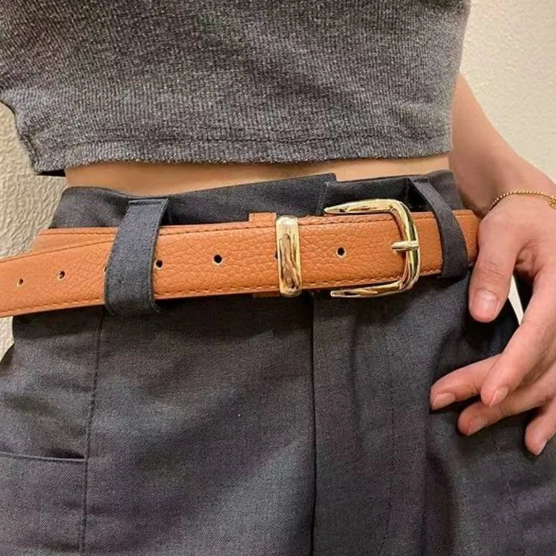 Nahaufnahme eines eleganten tanfarbenen Kunstlederschlüppchens mit goldener Schnalle über dunkelgrauer Kleidung.