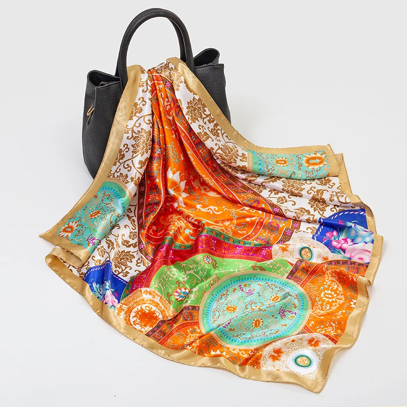 A luxury silk square scarf featuring vibrant orange, pink, and green patterns with gold trim.