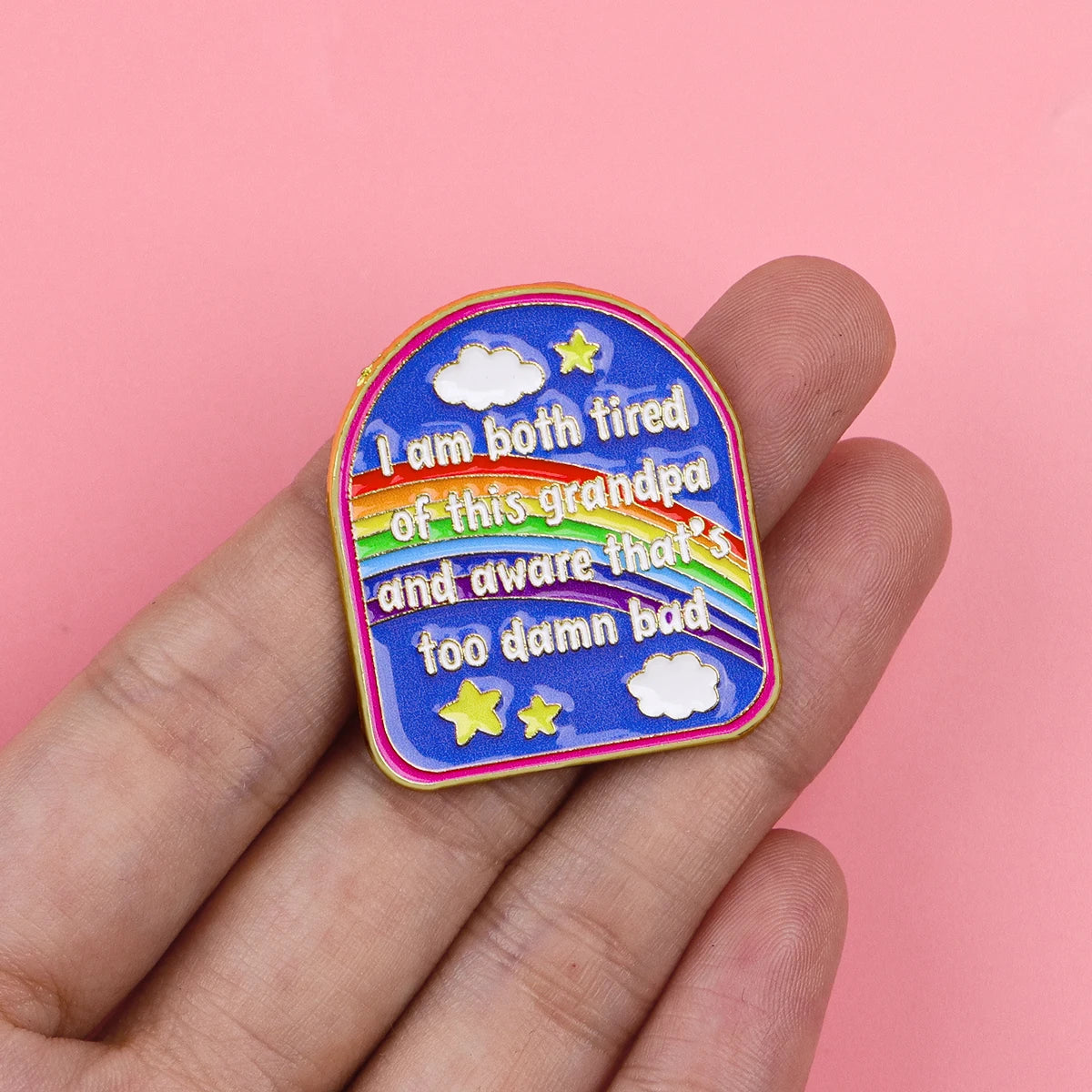A colorful enamel pin featuring text that reads I am both tired of this grandpa and aware that's too damn bad