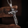 Silver retro Christian cross amulet necklace hanging from a chain on a dark brown rock.