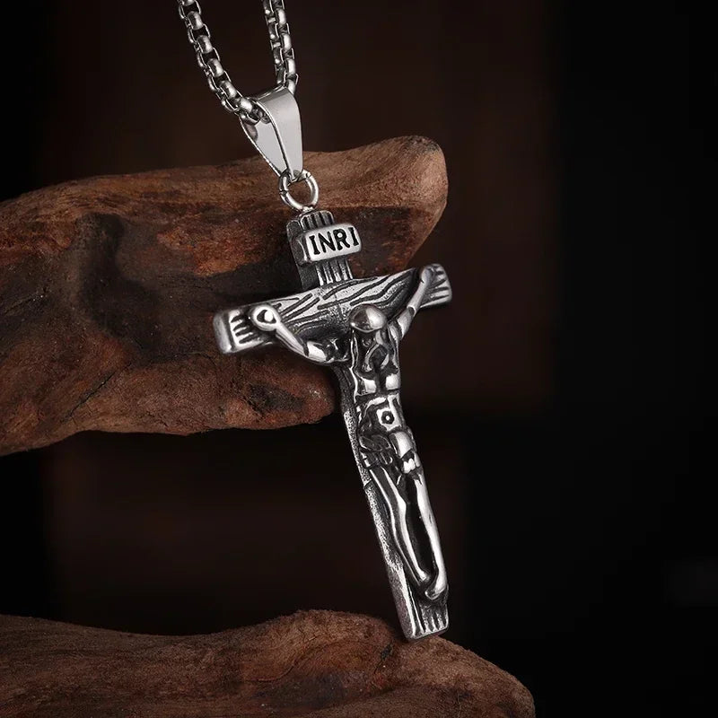 Silver retro Christian cross amulet necklace hanging from a chain on a dark brown rock.