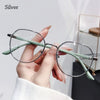 A hand holds a pair of silver anti-blue light metal eyeglasses with light green frames.