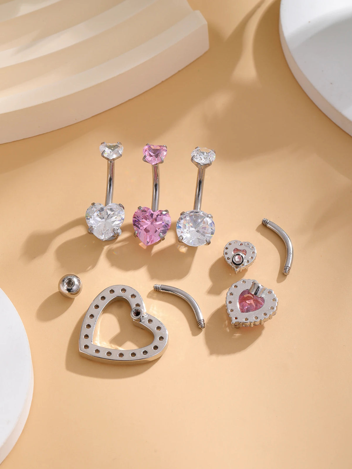 A set of five gold stainless steel dangled belly button rings featuring heart-shaped and round gemstone designs.