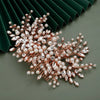 A delicate bridal headpiece featuring small pearls and clear rhinestones arranged in a floral spray against a dark green back