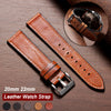 A brown leather watch strap with a silver buckle is displayed on a wooden surface, showing various leather colors.