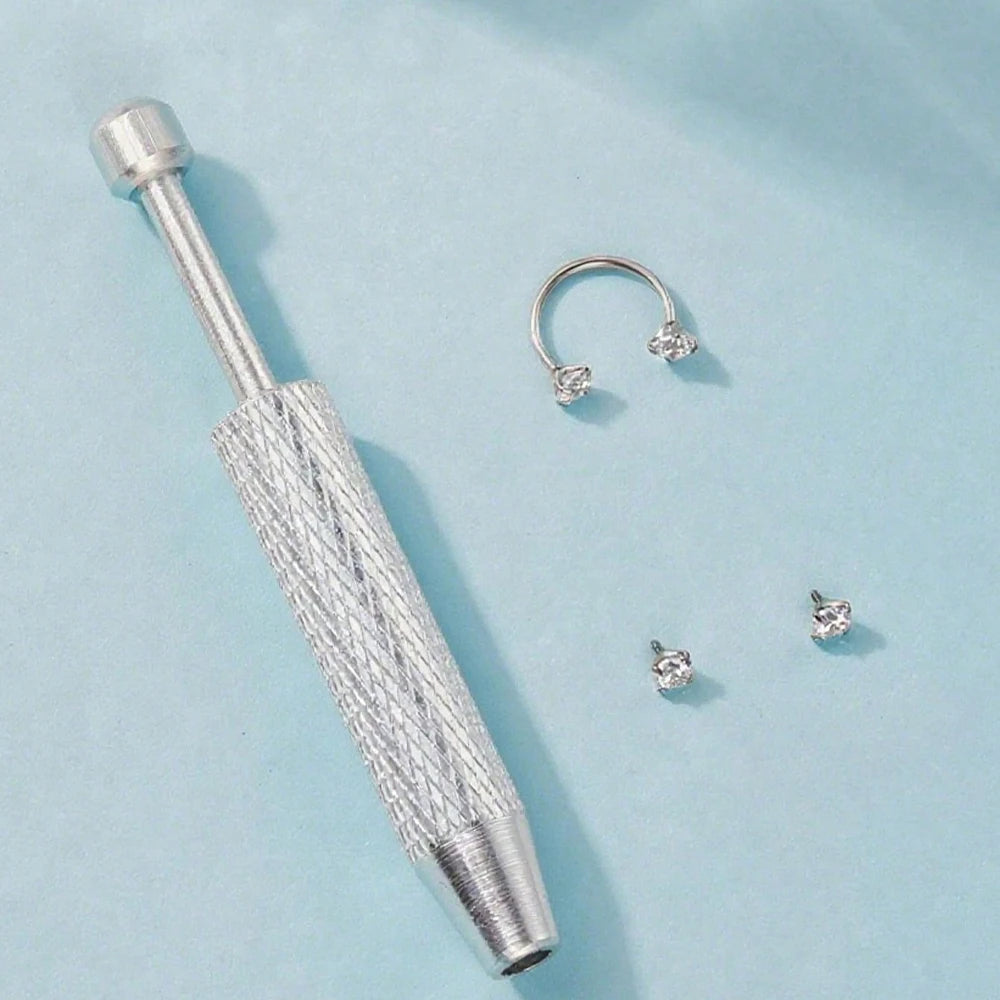 A silver stainless steel ball grabber tool with a hoop and several small stud earrings on a light blue background.