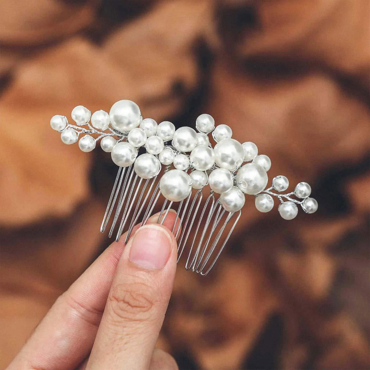 Une main tient une peigne de cheveux pour mariée en cristal et perles blanches.
