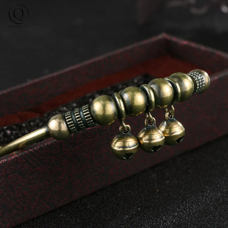 Vintage brass bell charm bracelet with gold-toned beads and dangling charms displayed in a dark red box.