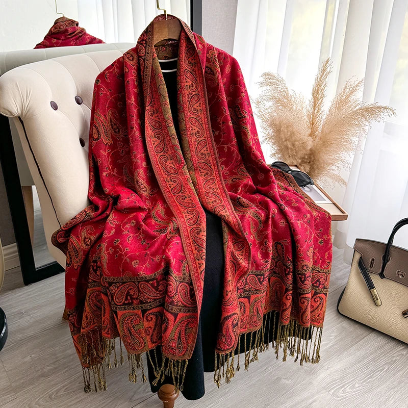 A vibrant red bohemian paisley tassel shawl draped over a hanger.