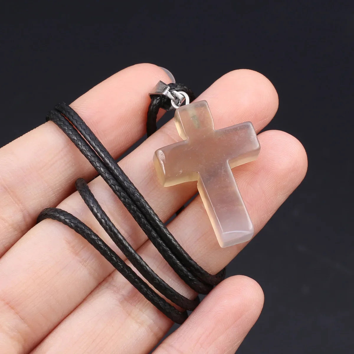 Klares, hellamberfarbenes Tigerauge-Agat-Kreuz-Anhänger auf einer schwarzen Leder-Kordel in der Hand.