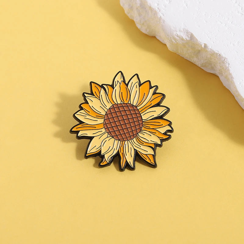 A small enamel flower brooch featuring a yellow sunflower design on a light yellow background.