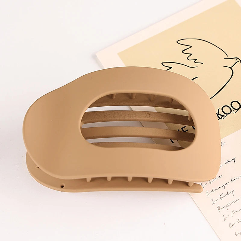 A beige flat circular hair clip set is shown resting on a piece of paper with a line drawing of a bird.