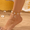 A close-up of a woman's ankle wearing a bohemian starfish conch anklet made of gold and white beads on a sandy beach.