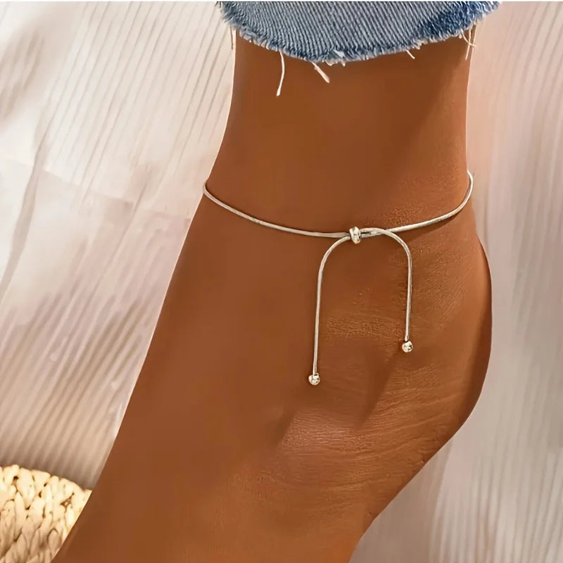 Pendentif de cheville argenté à tirer porté sur la cheville d'une personne.