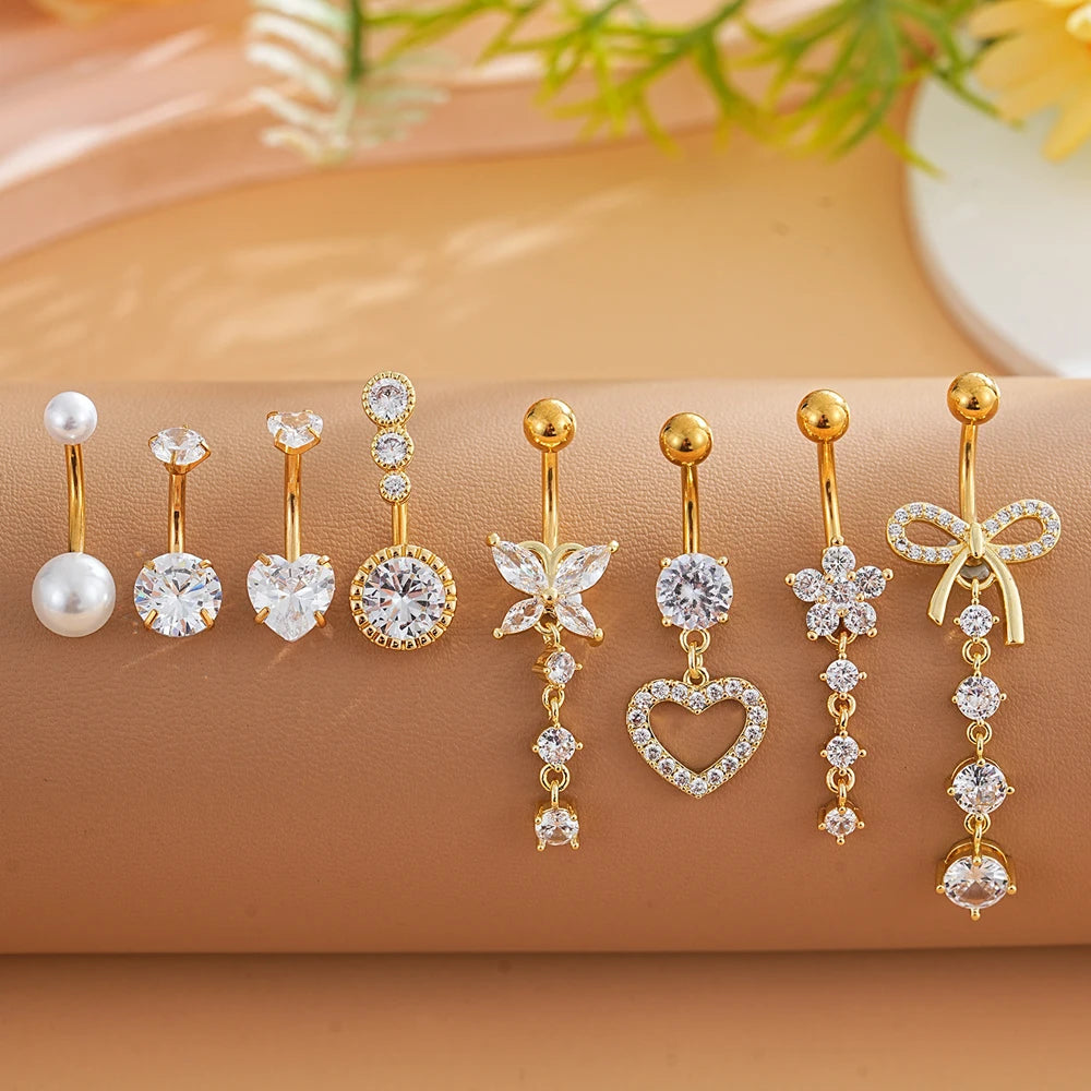 A set of gold dangle curved belly piercing jewelry featuring heart and flower designs on a beige background.