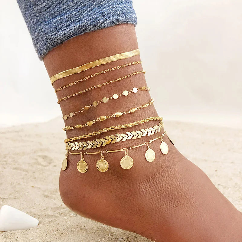 A close-up of a woman's ankle showing multiple layered gold snake chain anklets.