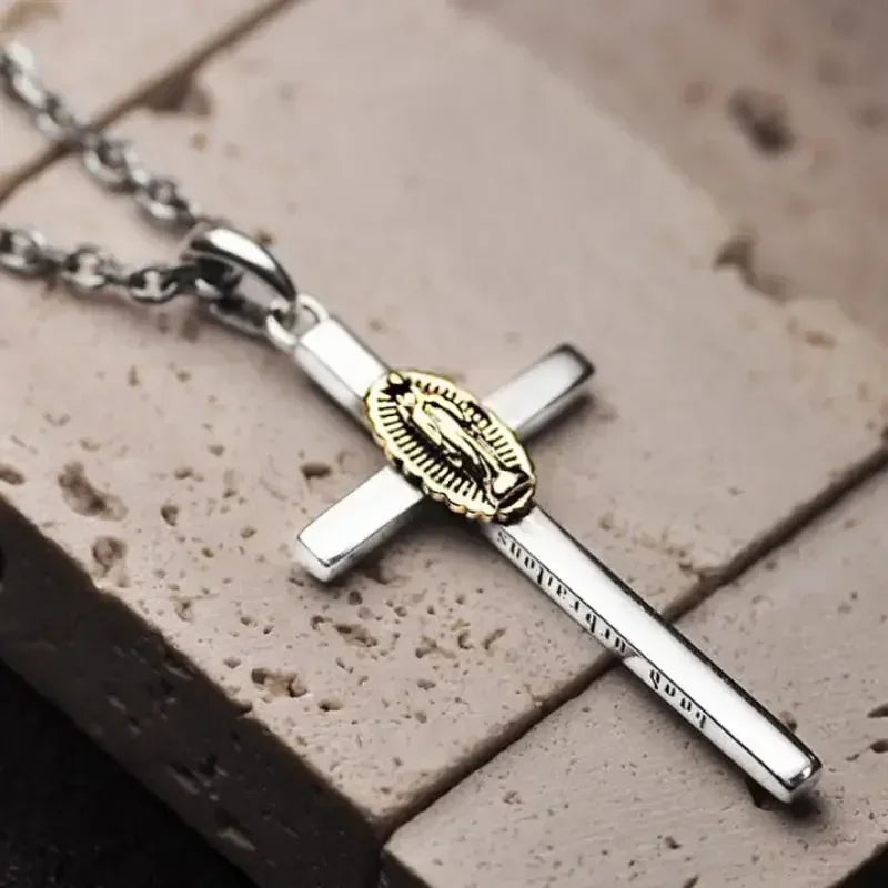 A silver cross amulet necklace with a gold-colored pendant resting on a light brown surface.