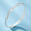 A silver twisted bangles bracelet worn on a wrist against a light blue background.