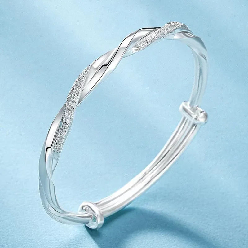 A silver twisted bangles bracelet worn on a wrist against a light blue background.
