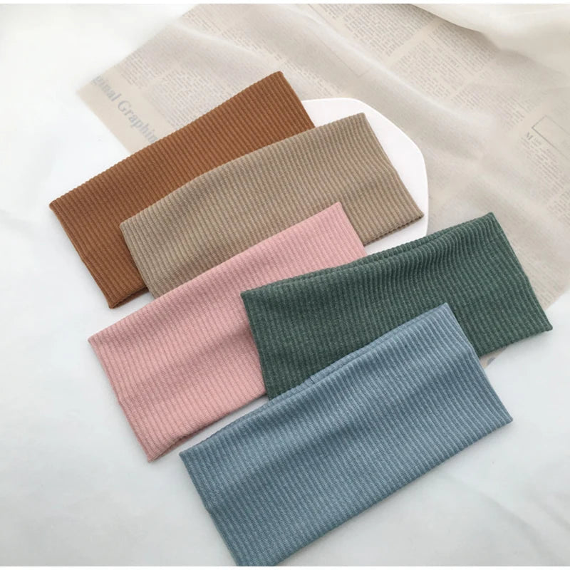 A collection of knitted sports headbands in various earth tones and shades of pink and green laid on a light fabric.