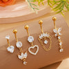 A set of five gold stainless steel dangled belly button rings with diamond accents displayed on a beige surface.
