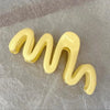 Pinza para el cabello en forma de ola de gel amarillo contra un fondo gris.