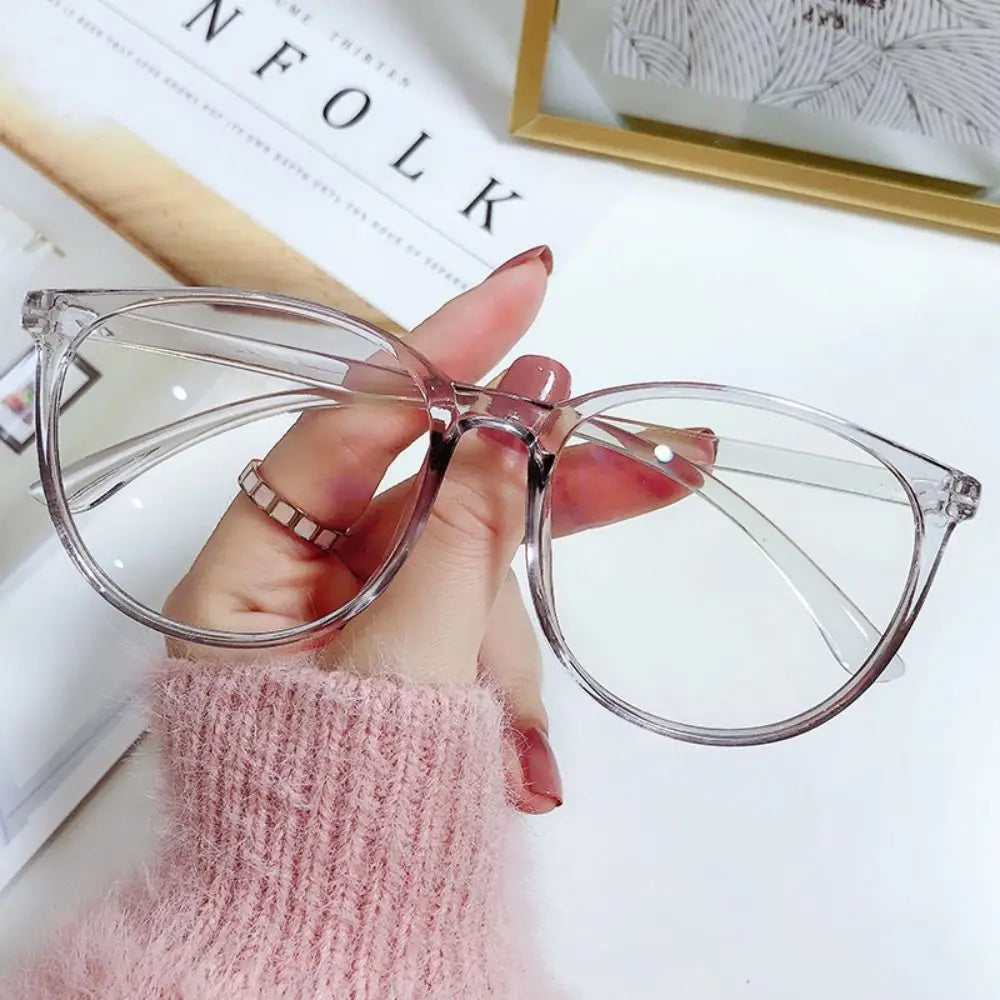 A hand holds a pair of clear, large square anti-blue light spectacles against a white background.