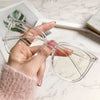 A hand holds a pair of clear, large square anti-blue light spectacles on a marble surface.