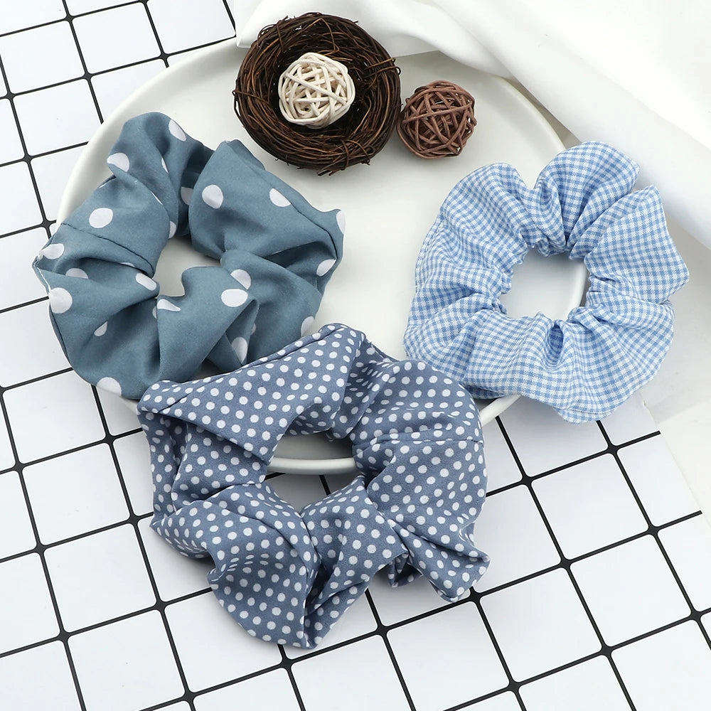 A flat lay of three fabric scrunchie headbands in blue and white patterns, along with two dark brown knitted balls.