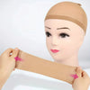 A hand is stretching a tan wig cap over a mannequin head.