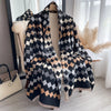 A black and beige plaid cashmere feel scarf draped on a mannequin in a bright room.